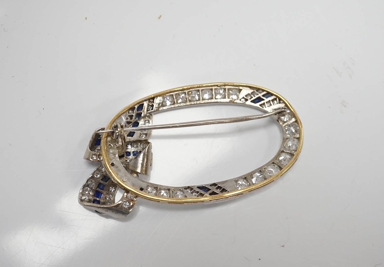 A yellow and white metal, sapphire and millegrain set diamond cluster oval open work brooch, with ribbon bow motif, 50mm, gross weight 11 grams. Condition - good